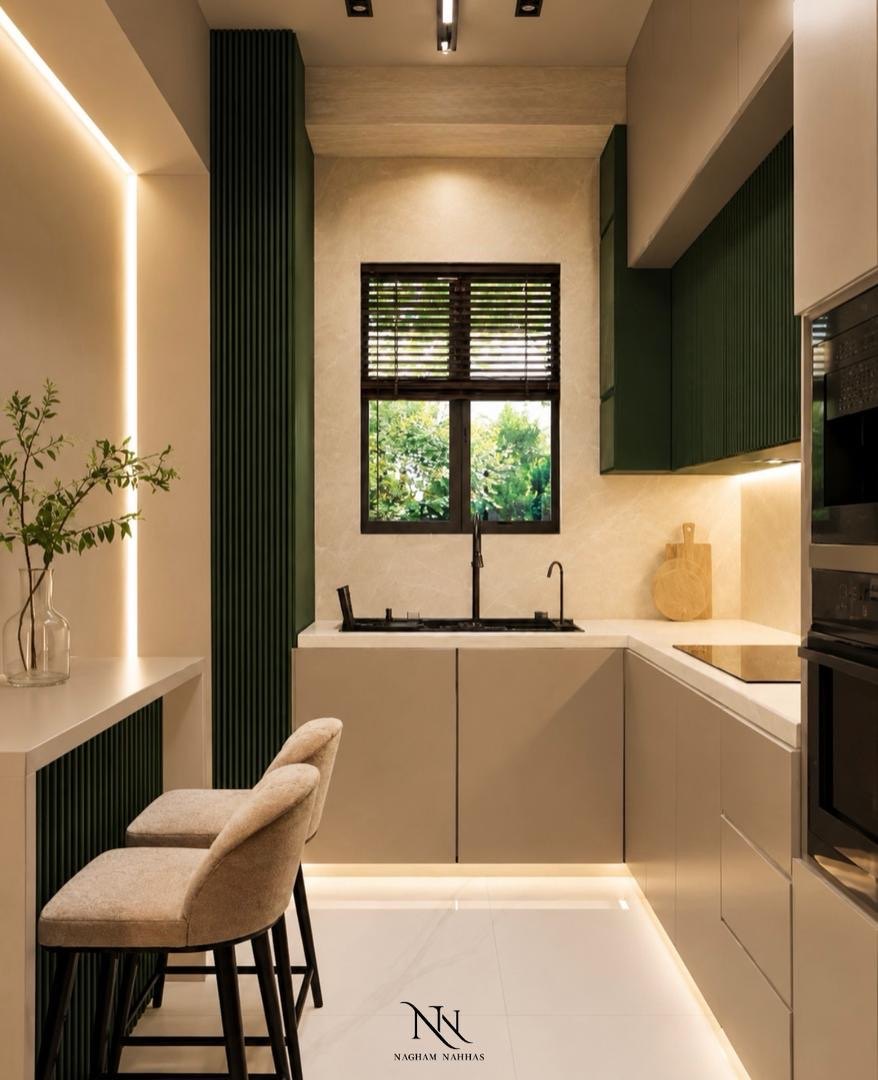 Narrow kitchen in deep green and stone with a window above the sink and two bar stools
